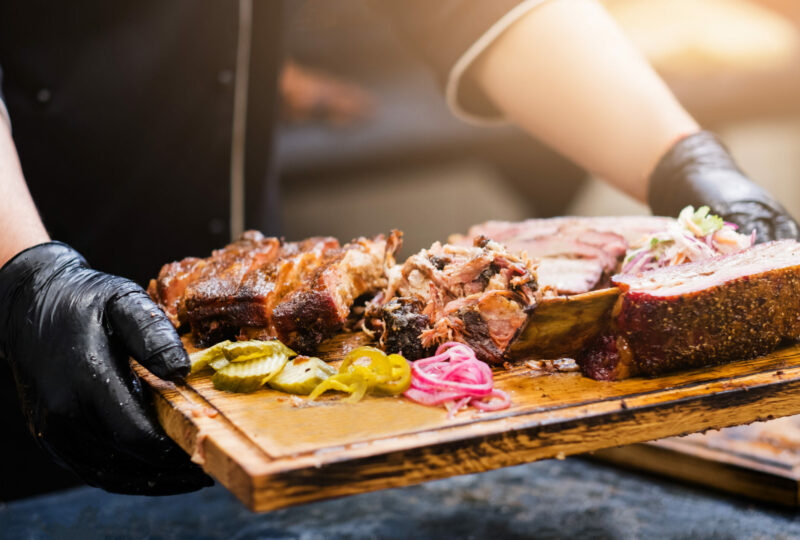 Professional catering. Cropped shot of chef holding wooden board with smoked meat assortment.